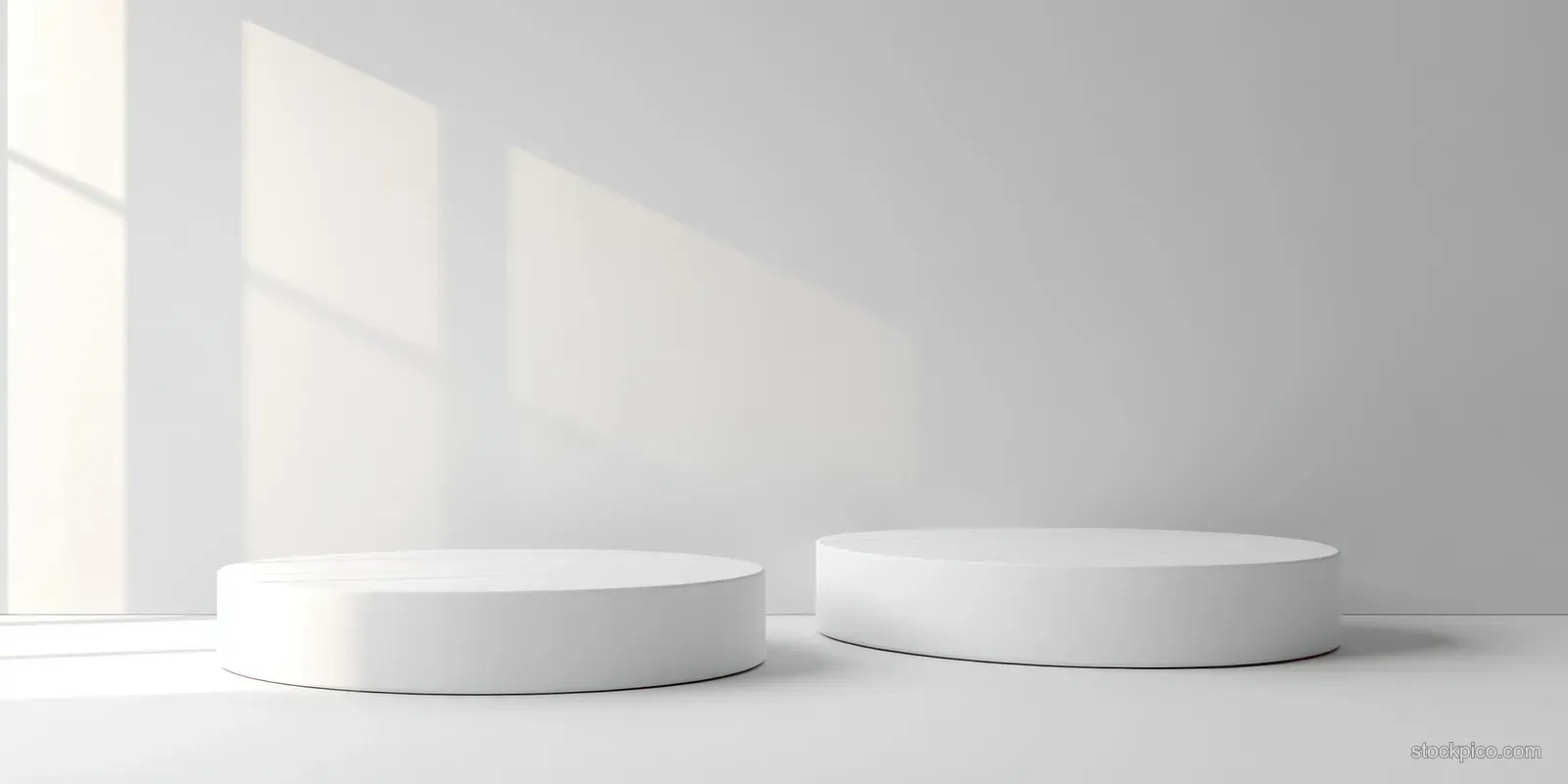 Minimalist white round podiums of different heights in a softly lit room with window pane shadows on the wall.
