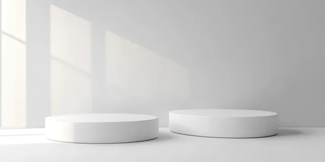 Minimalist white round podiums of different heights in a softly lit room with window pane shadows on the wall.