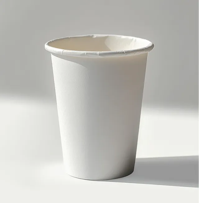 Empty white disposable paper cup on a white surface with a soft shadow from studio lighting.