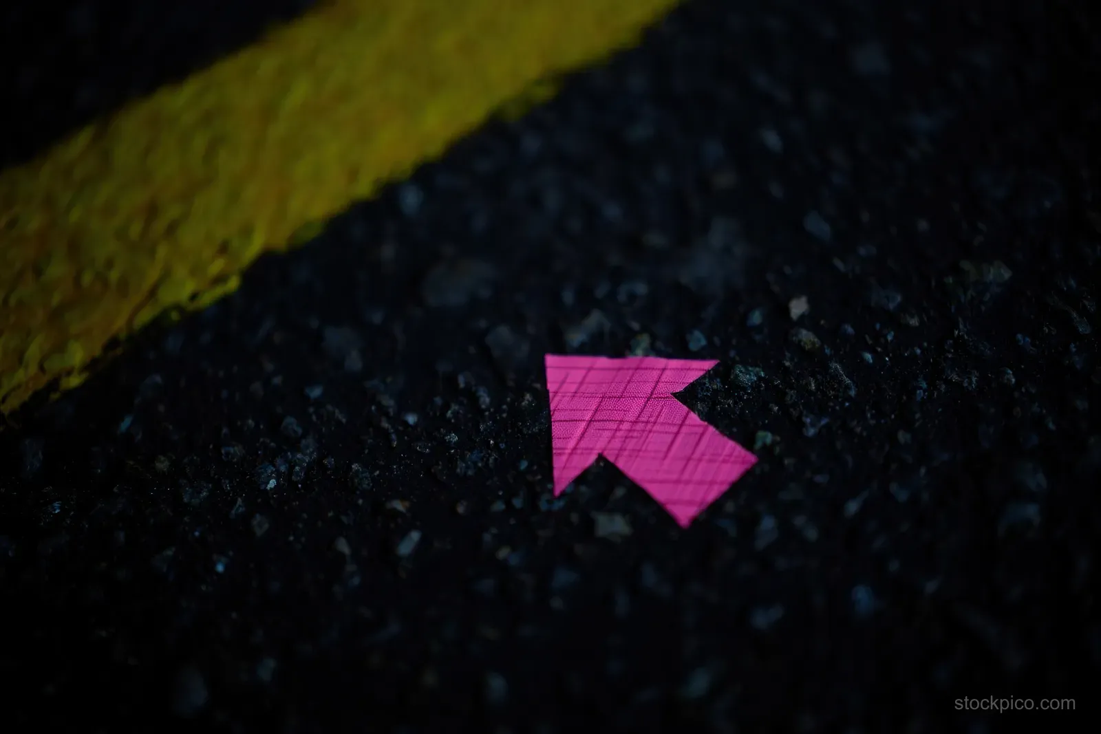 A small pink arrow sticker points on rough dark asphalt beside a yellow road line in low light.