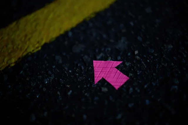 A small pink arrow sticker points on rough dark asphalt beside a yellow road line in low light.