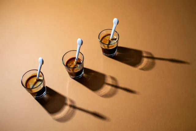 Three espresso glasses with white stir spoons on warm brown table, long shadows