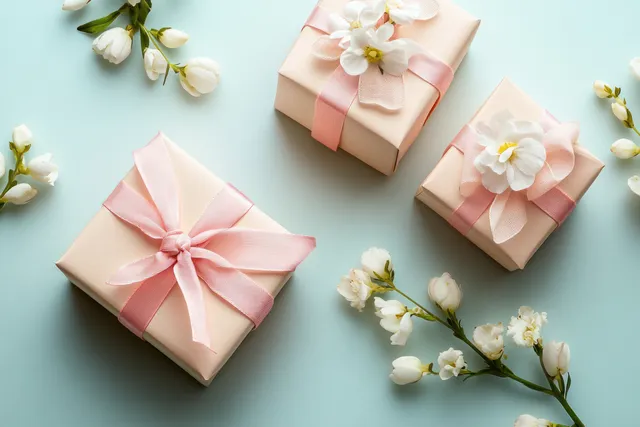 Top-down view of pink ribbon gift boxes with white blossoms on a beige background.