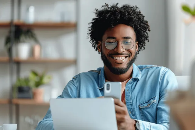 Cheerful young entrepreneur texting on smartphone while working at office desk