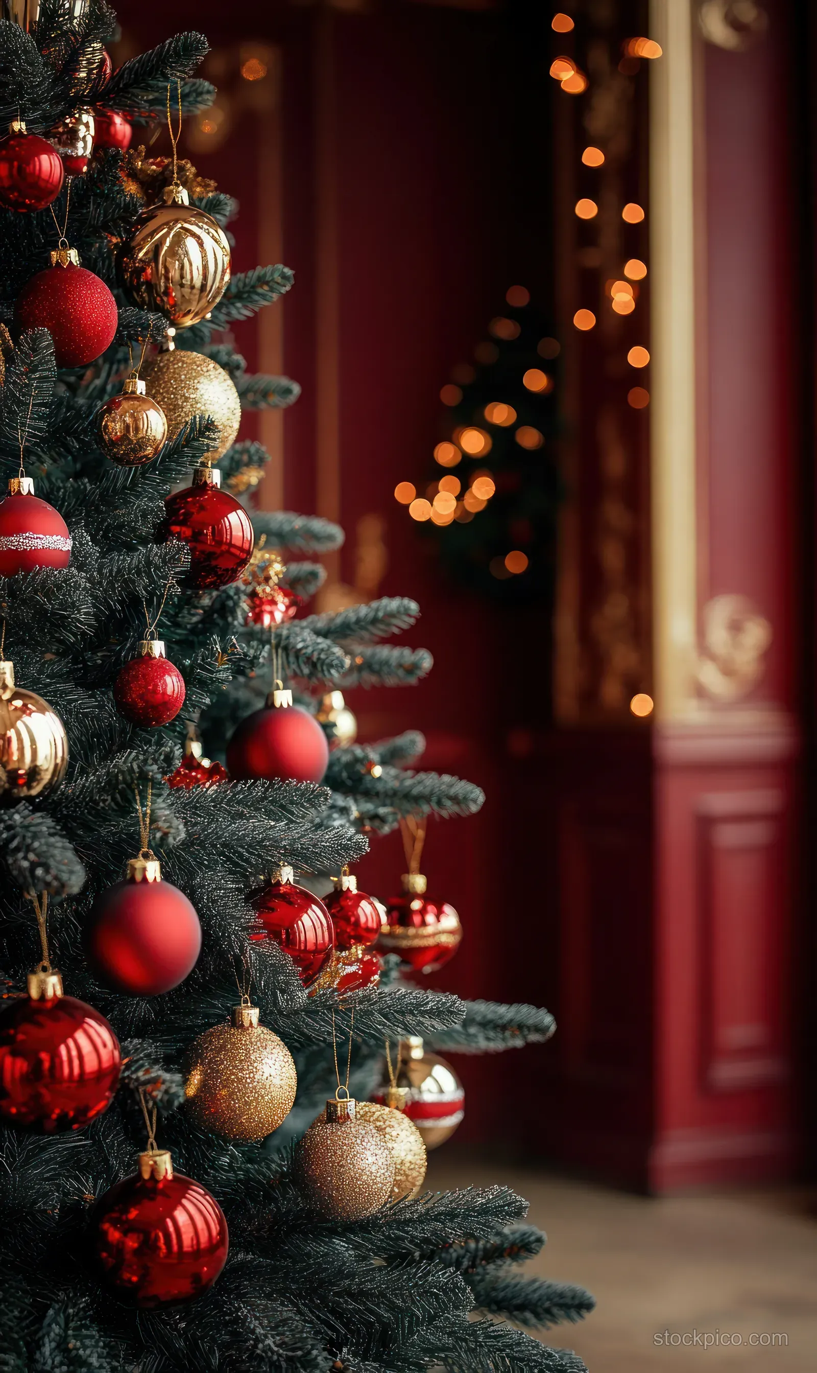 A decorated Christmas tree branch with red and gold ornaments beside warm blurred candlelight in a baroque room.