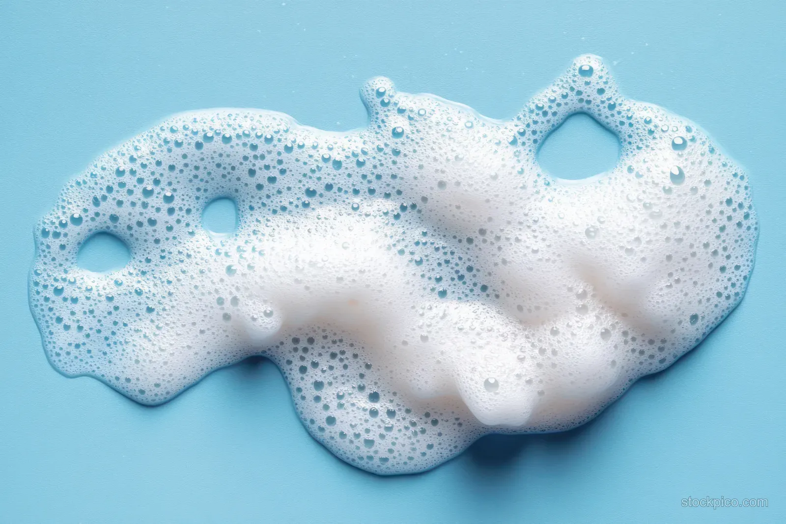 Lathered facial cleanser mousse foam rests on a blue background with many small bubbles visible.