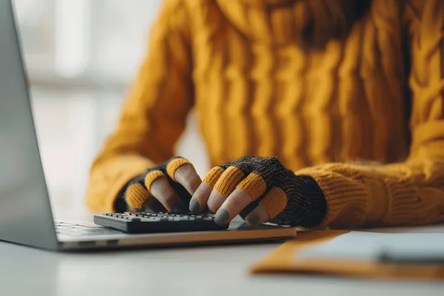 A woman’s hands type on a laptop at a desk beside financial documents and a chart.