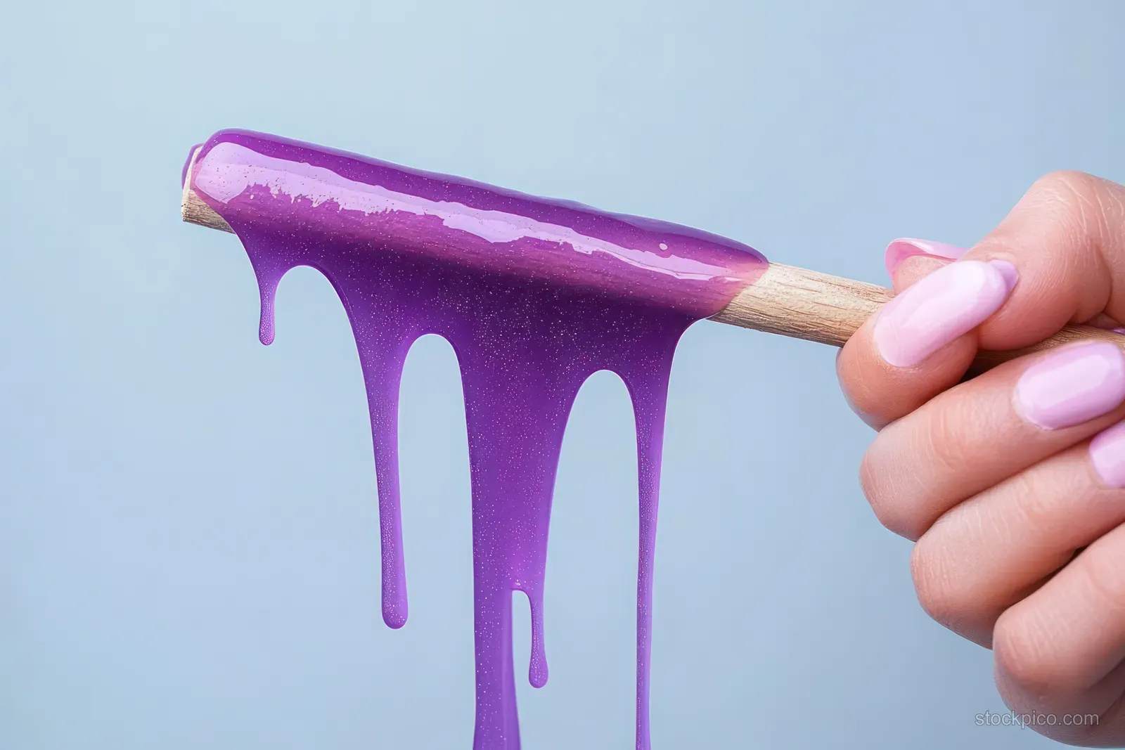 Hand holds a wooden waxing stick spreading thick purple wax drips on a blue background.