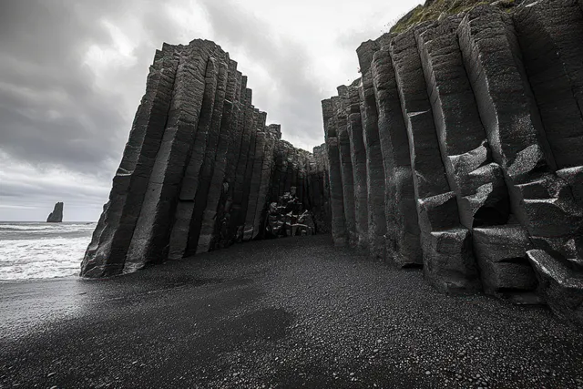 Dark hexagonal basalt columns rise from black sand beach, waves and stormy clouds