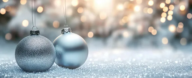 Silver Christmas ornaments hanging in snowy scene with warm bokeh lights