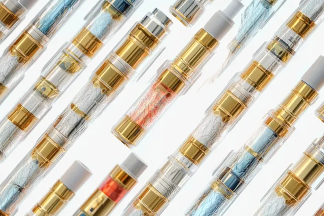 Transparent vaping cartridges with gold connectors and colored coils arranged diagonally on a white background.