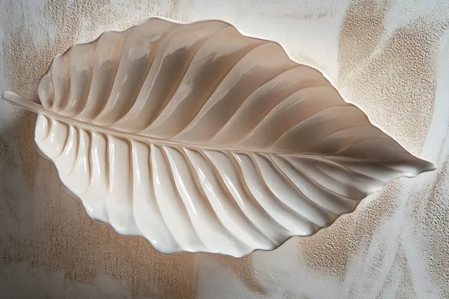 Pastel leaf sculpture resting on textured wall with soft sunlight and shadow