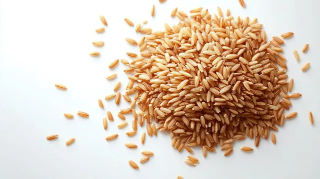 Uncooked brown rice grains scattered on a white surface with clear kernel texture.