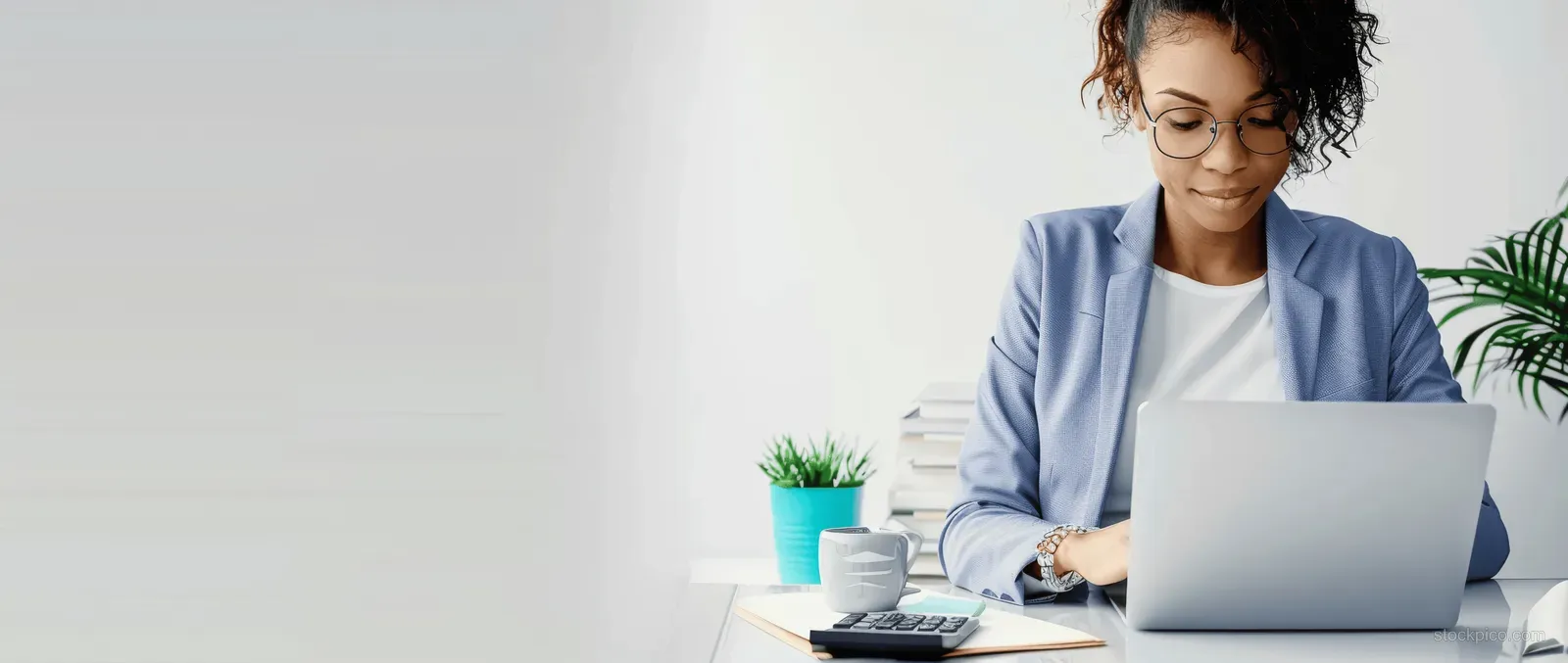 Businesswoman typing on a laptop at her desk next to a calculator and notebook with finance papers.