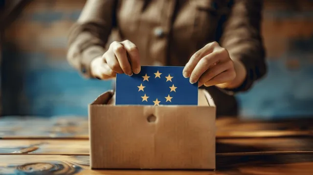 A woman’s hands drop a ballot into a cardboard ballot box with an EU flag sticker visible.