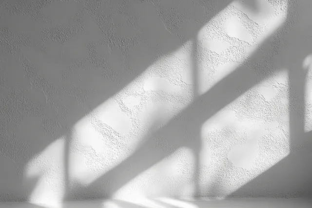 Sunlit window shadows stretch across a textured white wall with soft geometric light patterns