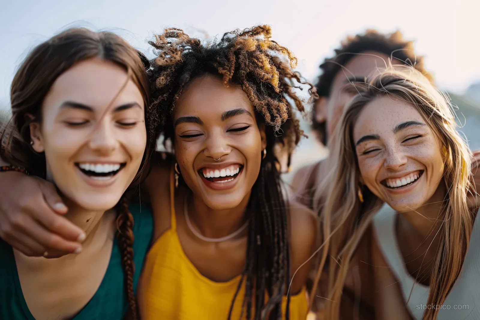 Three diverse women hug and laugh together outdoors with warm sunlight and city street blur behind them.