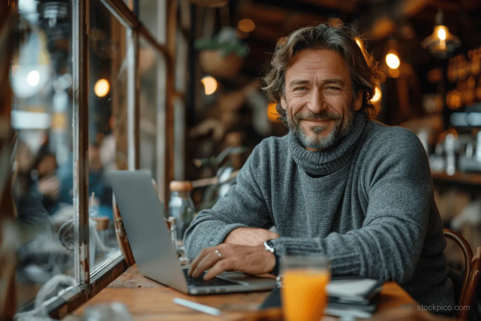 An entrepreneur types on a laptop in a cafe while a smartphone and glass of orange juice sit on the table.