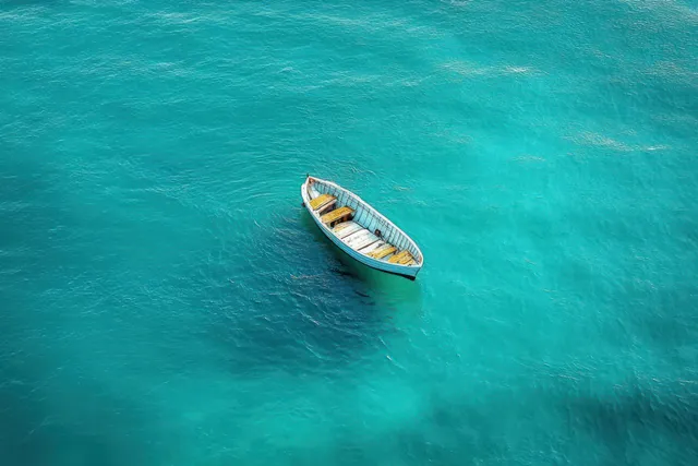 A small empty wooden rowboat floats alone on clear turquoise water with gentle ripples.
