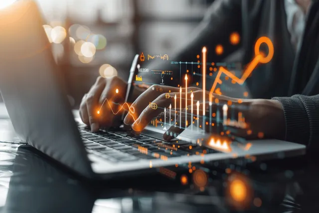 A businessman reviews floating augmented reality finance charts over a laptop screen in an office.