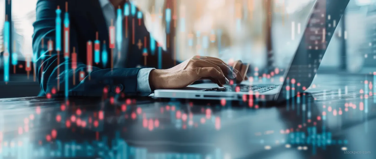 Man’s hands operate a laptop and tablet as glowing candlestick stock charts fill the background.