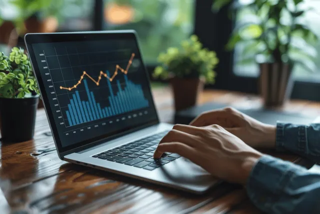 Analyst taps laptop growth chart with upward arrow while reviewing financial data at desk