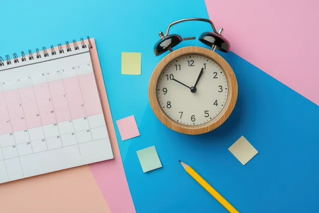 Spiral calendar and classic alarm clock near 12 with sticky notes and yellow pencil