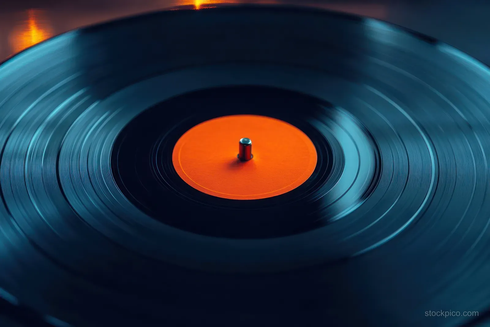 A vinyl record spins on a turntable with an orange center label under dramatic lighting.