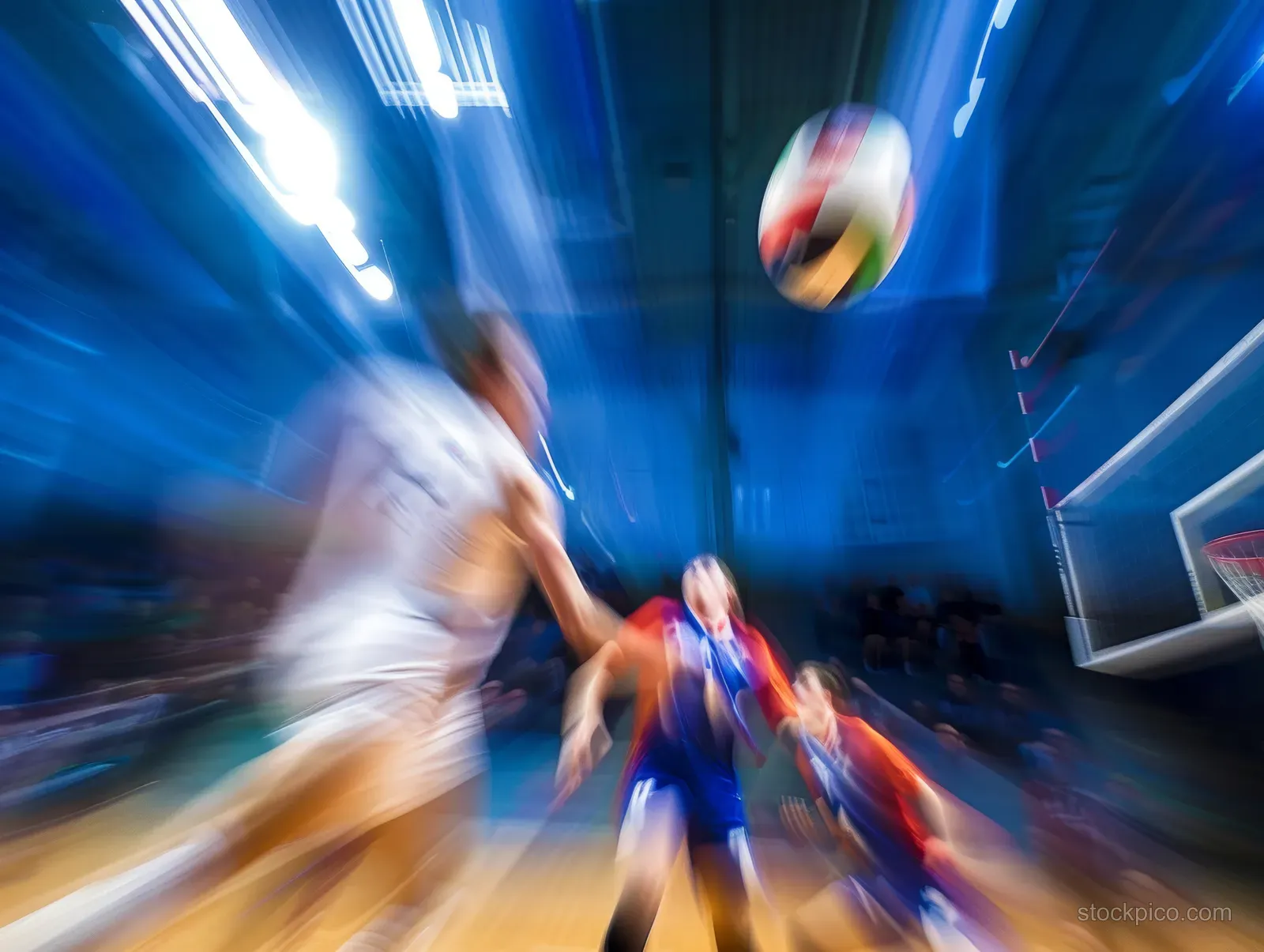 A volleyball spins in midair above an indoor court with players blurred by motion.