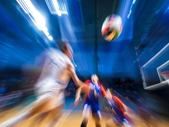 A volleyball spins in midair above an indoor court with players blurred by motion.
