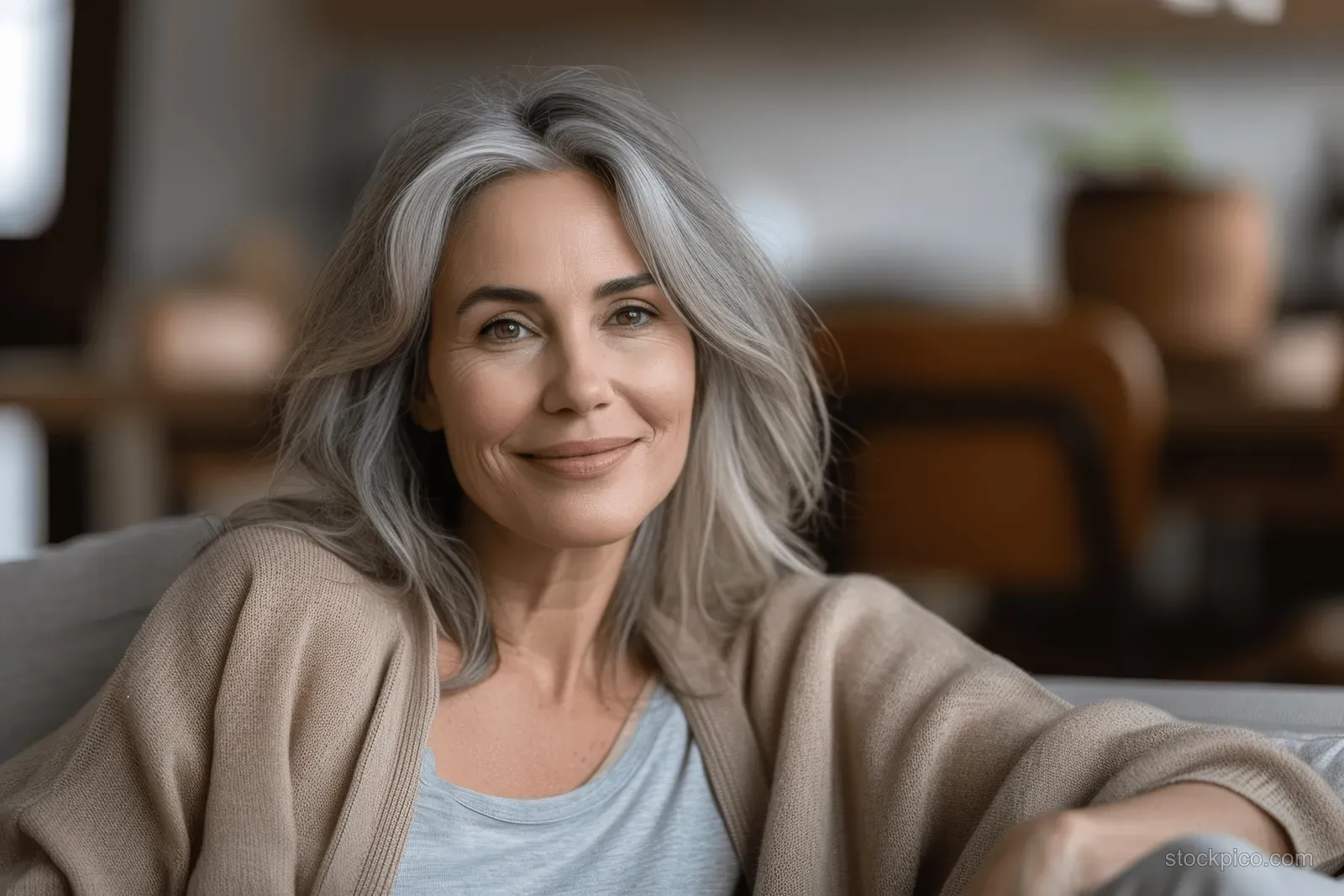 Smiling mature woman relaxing on a couch in a warm living room, looking directly at the camera.