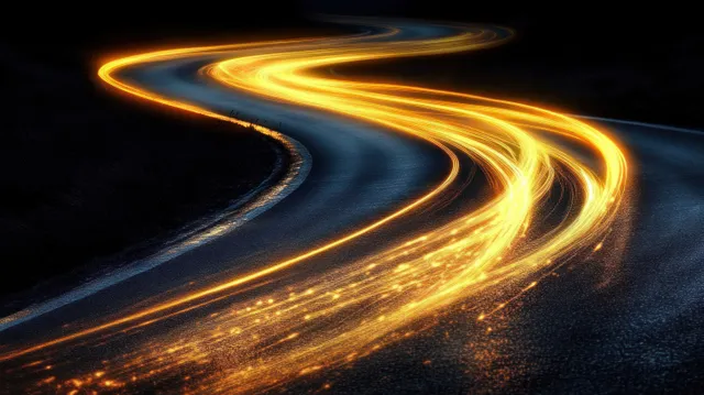 Golden light trails trace a winding road at night across dark asphalt, captured with long exposure.