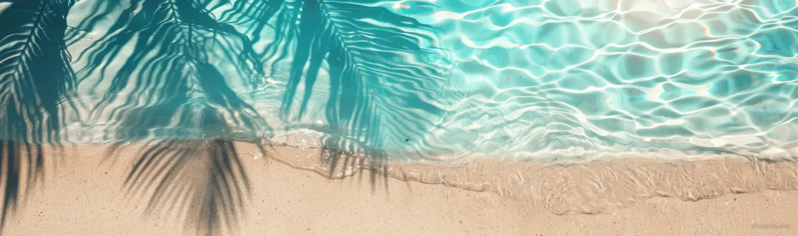 Top view of turquoise ocean water and palm leaf shadow on a sandy beach with clear copy space.