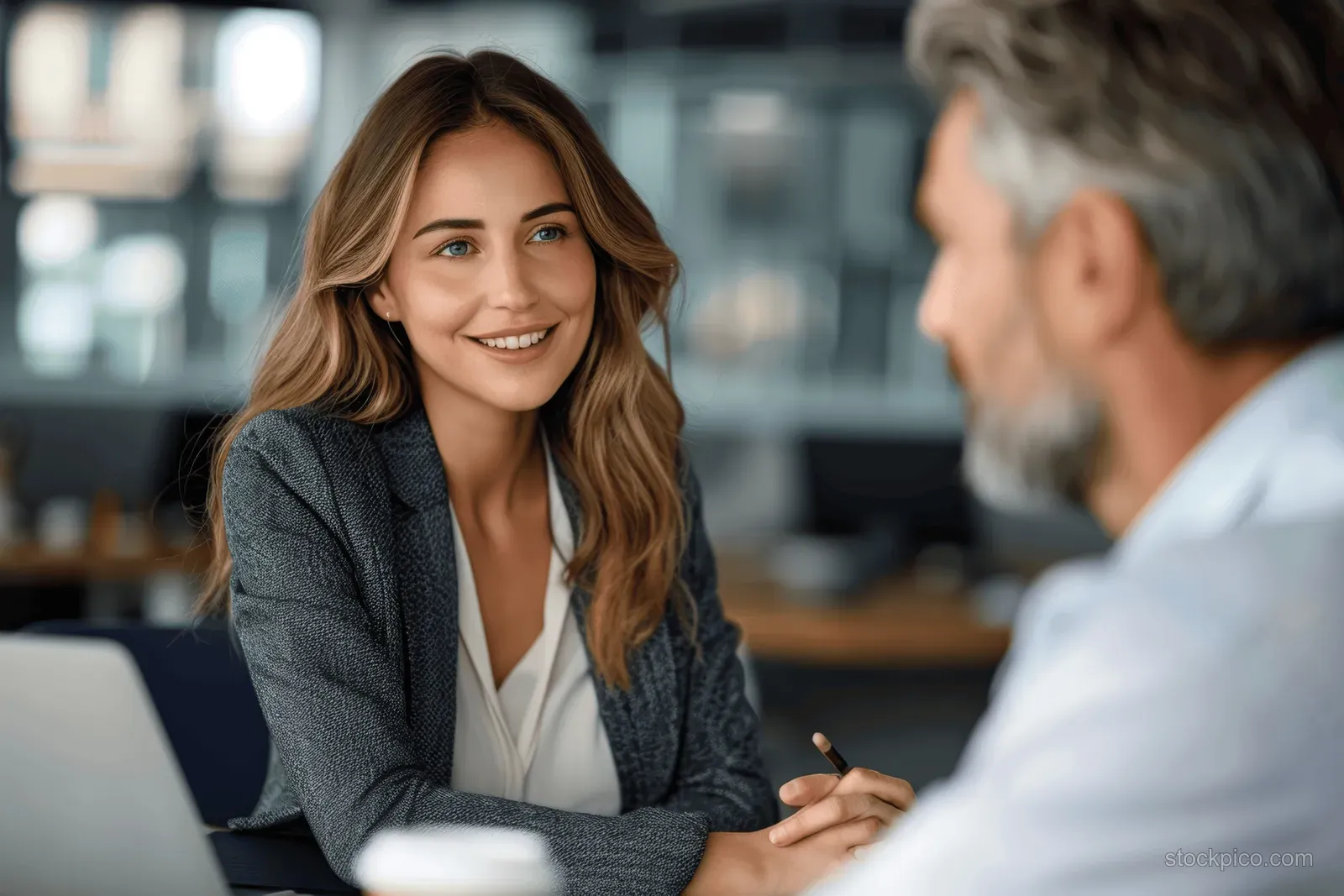 Mature businesswoman smiles while discussing a project on a laptop with a gray-haired businessman in an office.