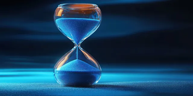 An hourglass close-up with blue sand pouring into the lower bulb on a dark blue background.