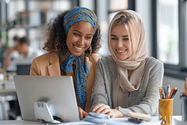 Two businesswomen collaborate on a laptop during a meeting in a bright office