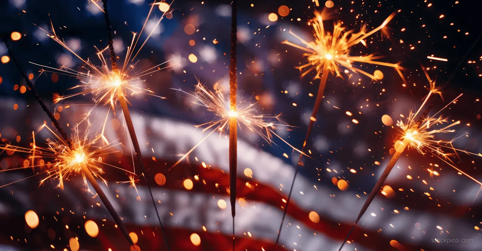 Sparklers flare in front of an American flag close-up with red and white stripes and glowing bokeh lights.