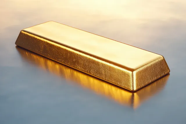 A shiny gold bar rests on a smooth reflective surface with warm light glowing along its edges.
