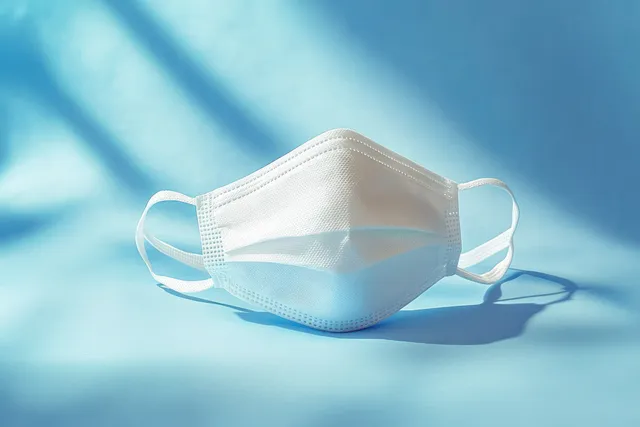 White disposable face mask lying on blue surface with soft natural light shadows with Personal Protective Equipment