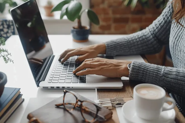 Closeup of hands typing on a laptop keyboard at a home office desk, illustrating remote work and digital productivity.