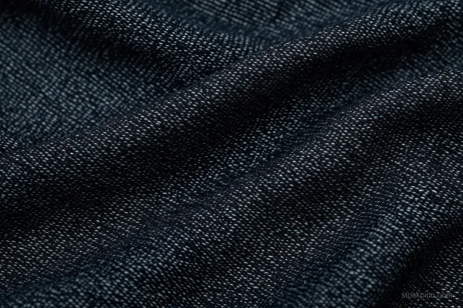 Macro close-up of dark woven fabric with thread pattern and subtle folds creating shadows.