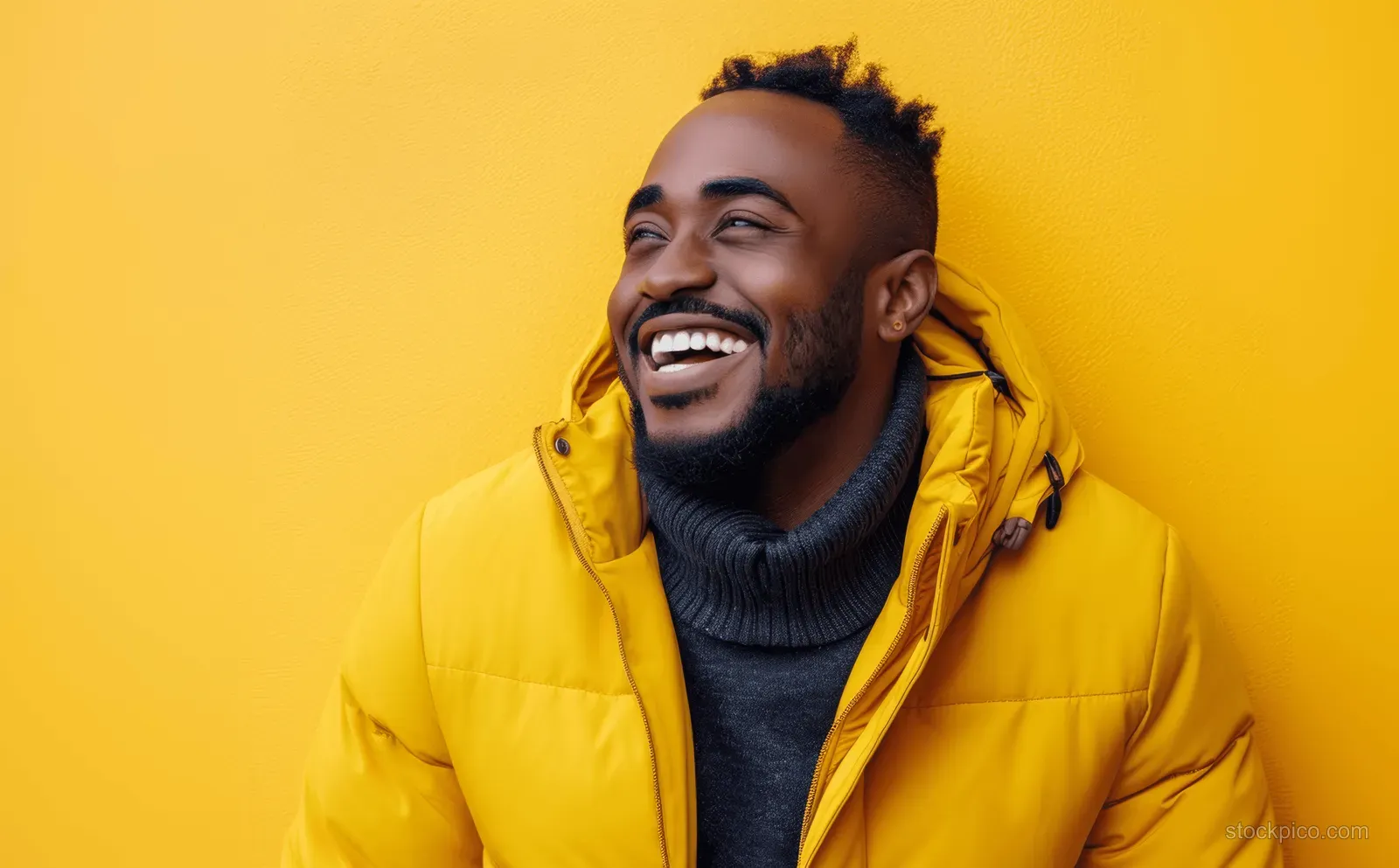 A laughing man in a yellow jacket against a solid yellow background, showing beard and teeth.