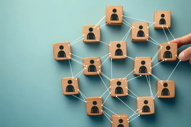 Wooden person blocks connected by lines on a blue background, with a hand adjusting one block to represent social networking.