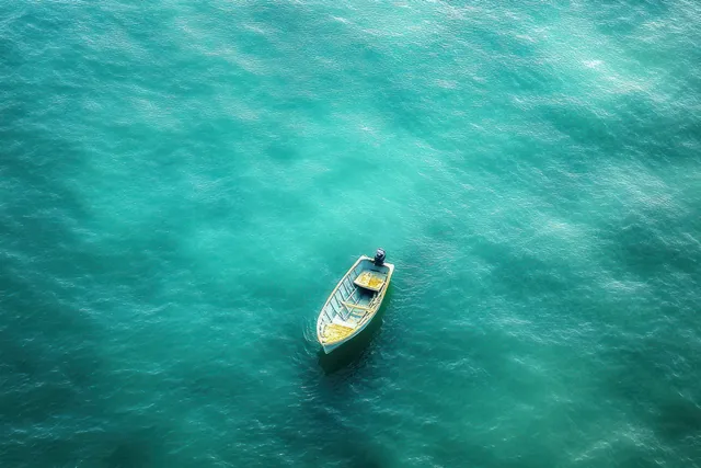 Overhead view of a small motorboat floating alone on calm turquoise water with gentle ripples.