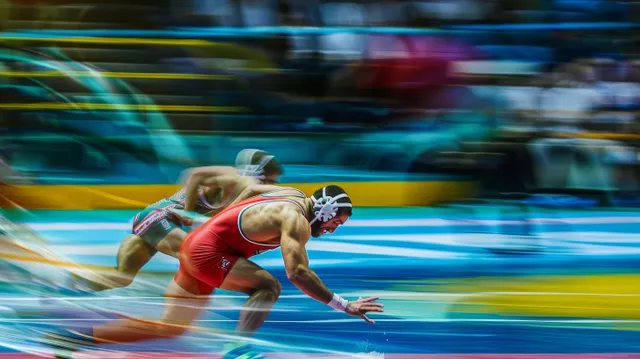 Two freestyle wrestlers grapple on a brightly colored mat as crowd lights blur behind them.