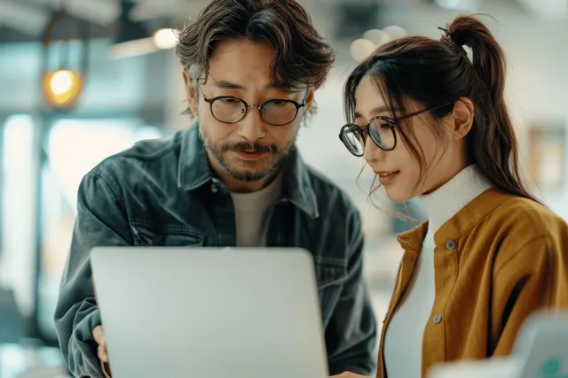 Male designer in glasses presenting a laptop to Asian coworker in a modern office