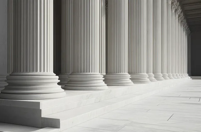 Fluted white marble columns with ornate capitals line a bright stone corridor with patterned floor tiles.