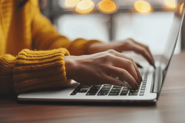 Woman’s hands type on a laptop keyboard on a white desk in a softly lit office.