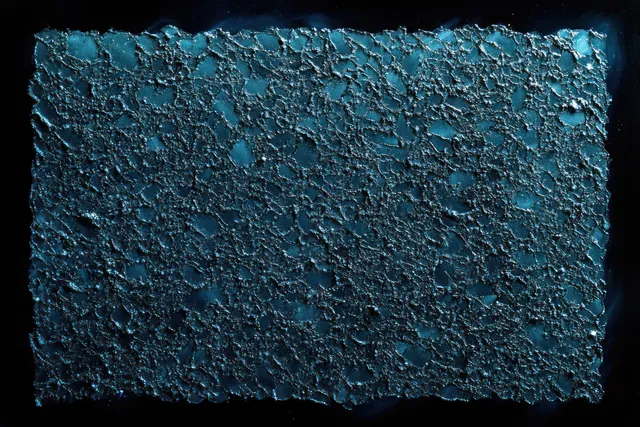 A cracked, pitted metal plate surface illuminated by blue light against a dark background.