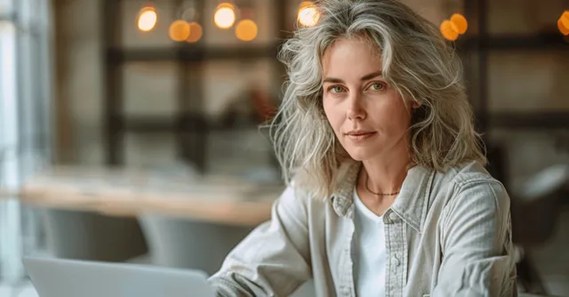 Smiling senior woman with silver hair seated indoors, looking toward camera with soft light